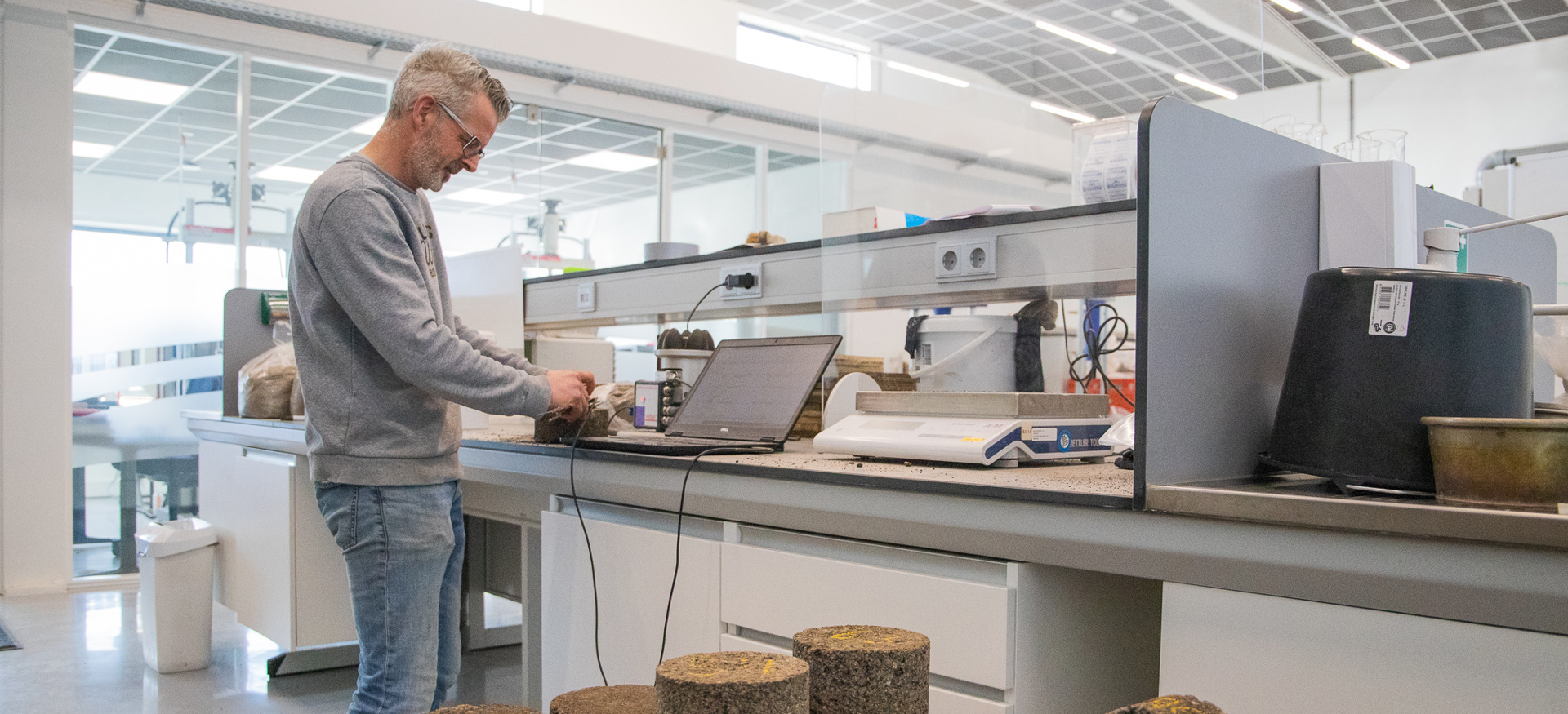 Man staat aan werkbank met laptop naast een aantal asfalt samples